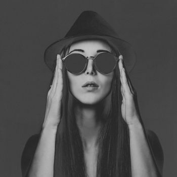 Beautiful young woman with long hair in round sunglasses and hat. Fashion and beauty. Image with negative, film grain effect