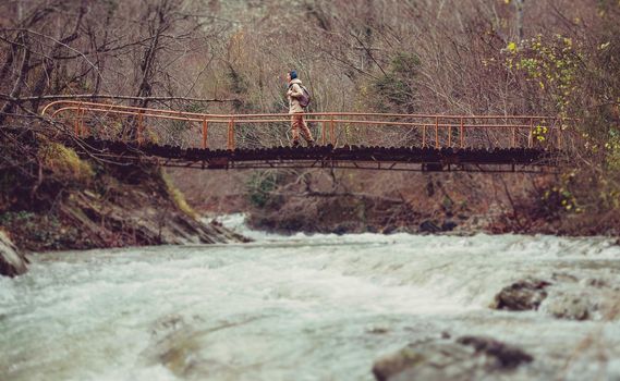 Hiker young woman crossing mountain river on a bridge in forest
