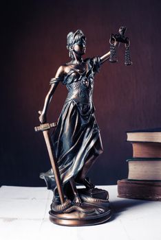 Themis figurine stands on a white wooden table next to a stack of old books. Scales Law Lawyer Business Concept. - Image