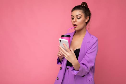 Young sexy positive woman isolated over pink background with copy space holding coffee to take away and a mobile phone.