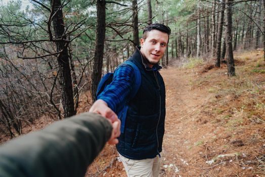 Hiker young man holding woman's hand and leading her in the forest outdoor. Point of view shot. Smiling man looking at camera