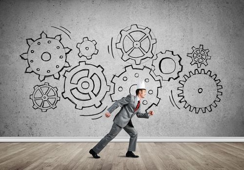 Young handsome businessman wearing white paper crown running and gear mechanism on wall