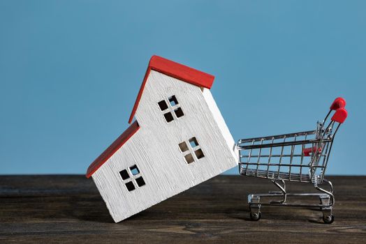 Model house and shopping cart on a blue background. Buying home, mortgage concept.