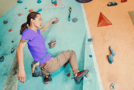 Free climber young woman training on artificial boulder wall indoors