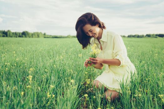 Smiling beautiful young woman picking yellow wildflowers on meadow in summer