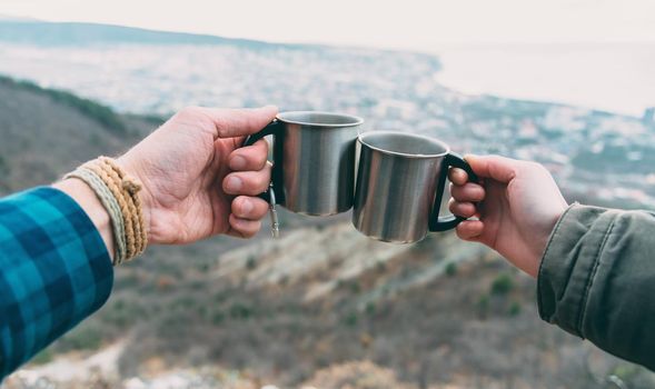 Hiker couple drinking tea in the mountains. View of hands with cups outdoor. Point of view shot