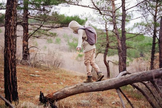 Traveler girl wearing in jacket hood and cargo pants with backpack walking on tree trunk in the forest