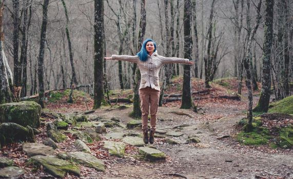 Happy young woman with blue hair jumping in autumn forest