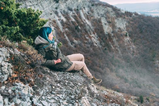 Young woman wearing parka jacket and cargo pants resting in the mountains and looking into the distance