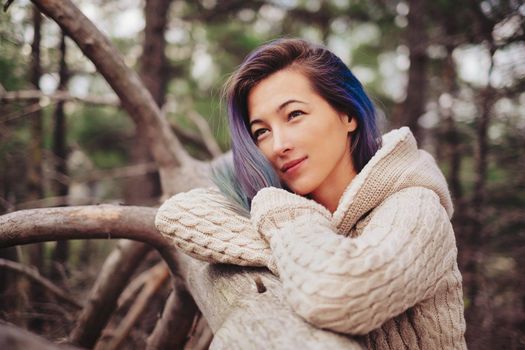 Beautiful young woman with blue hair standing near a tree and looking dreamy into the distance