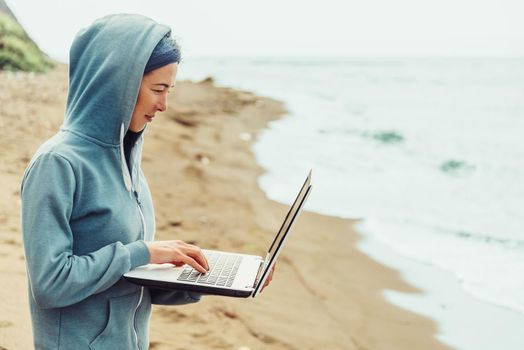 Freelancer young woman working on laptop on shore near the sea. Freelance concept