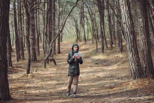 Hiker young woman walking on path with digital tablet in the forest. Concept of technology and travel