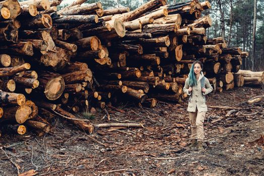 Hiker young woman with backpack walking near stack of tree trunk in the forest