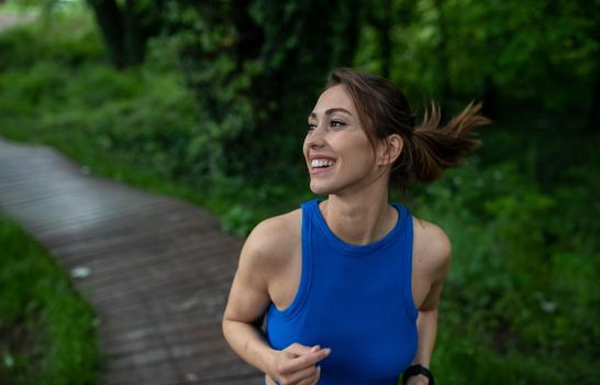 Active young jogger exercising in nature smiling. Portrait of female athlete running down path in park. 