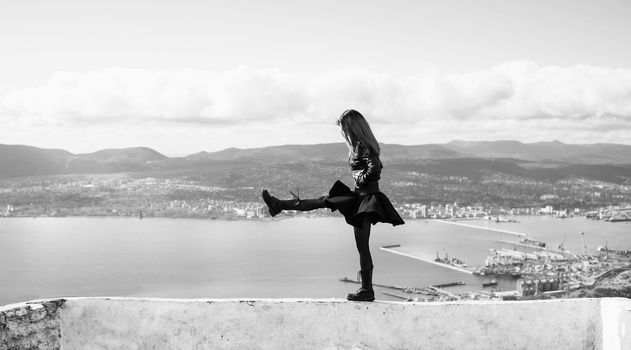 Young woman walking on high edge over the sea bay. Black and white image