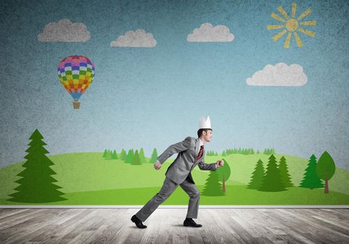 Young handsome businessman wearing white paper crown running in a hurry