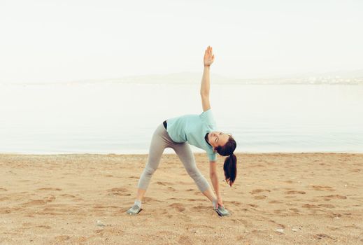 Sporty young woman stretching on sand beach in summer, workout. Concept of healthy lifestyle