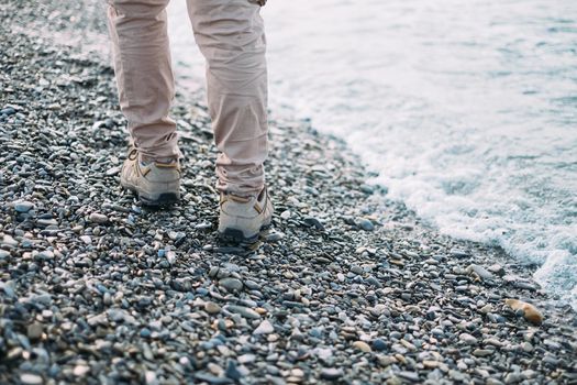 Unrecognizable woman walking on pebble coast near the sea, view of legs. Rear view