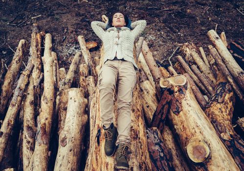 Beautiful young woman with blue hair lying on stack of felled tree trunk. Hiker girl resting outdoor