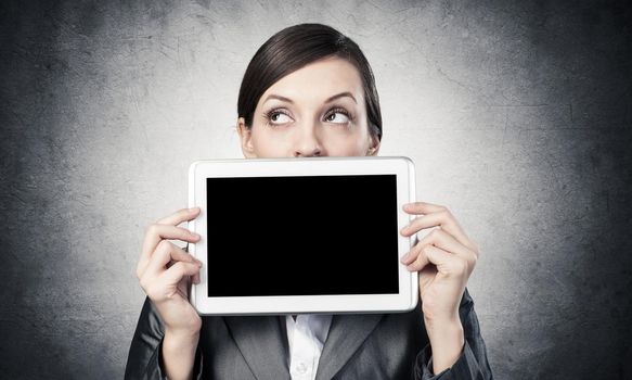 Businesswoman holding tablet computer with blank screen. Beautiful woman in business suit show tablet PC near her face. Corporate businessperson on grey wall background. Digital technology layout.