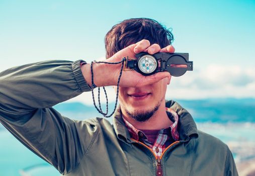 Smiling young man holding compass on background of sea outdoor