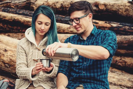 Traveler loving couple resting outdoor. Young man pouring tea from thermos to cup of young woman