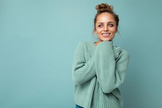 Young beautiful cute curly blonde woman with sexy expression, cheerful and happy face wearing trendy blue sweater isolated over blue background with copy space.