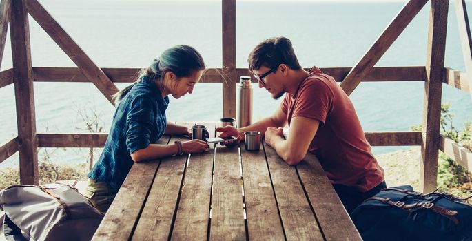 Young loving couple resting in arbor and looking something at smartphone in summer outdoor