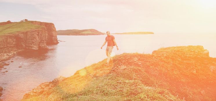 Hiker young man walking on coastline near the sea in summer. Image with sunlight effect