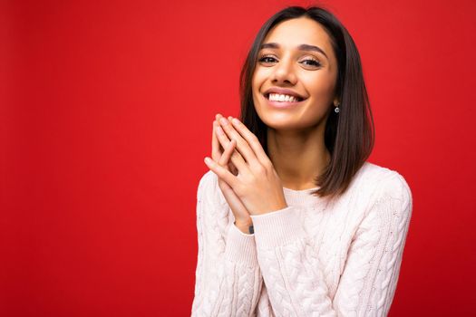 Positive cheerful cute smiling young brunette woman in casual sweater isolated on red background with copy space.
