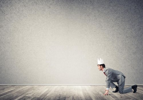 Young handsome businessman wearing white paper crown running in a hurry