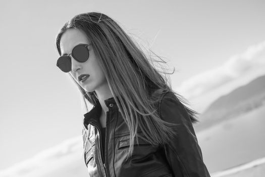 Monochrome portrait of fashionable girl wearing in leather jacket and round sunglasses outdoor