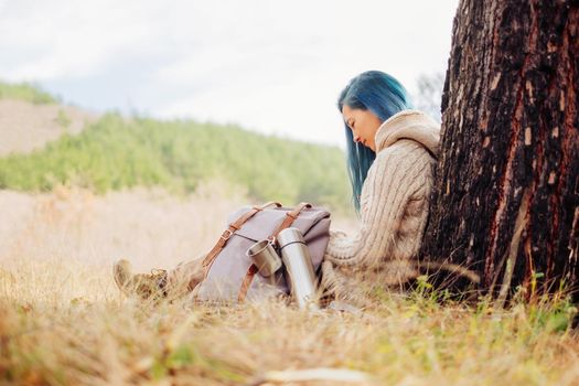 Traveler young woman with backpack and thermos sitting near the tree outdoor in spring