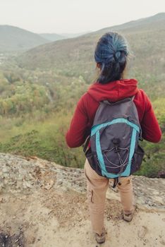 Hiker young woman with backpack standing on rock and looking at mountains, rear view