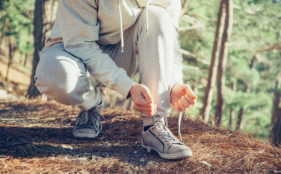 Unrecognizable sportsman runner tying shoelaces outdoor near the tree at sunny day