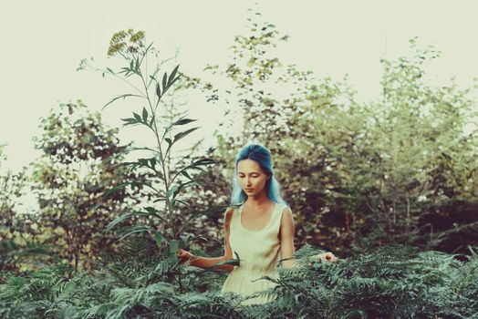 Beautiful girl with blue hair walking in fairy forest, girl standing near a big flower. Toning color