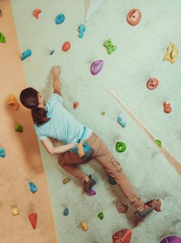 Free climber young woman coating her hand in powder chalk magnesium and climbing artificial boulder indoors