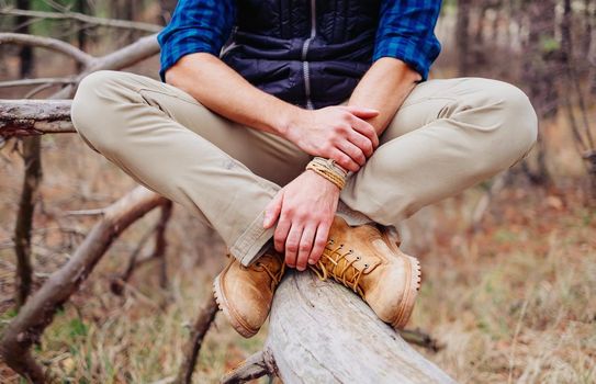 Unrecognizable traveler young man sitting on tree trunk, view of legs