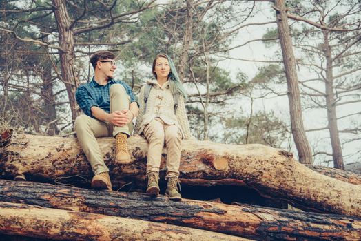 Hiker young loving couple sitting on felled tree trunks in the forest. Couple resting outdoor