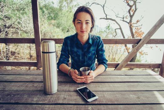 Young woman resting in wooden veranda in summer outdoor, looking at camera. Girl has a picnic in arbor