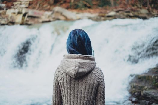 Traveler woman with blue hair looking at beautiful waterfall, rear view