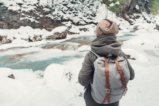 Traveler young woman with backpack standing in front of river in winter