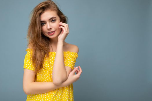 Young attractive blonde female person with sincere emotions isolated on background wall with copy space wearing summer yellow dress. Positive concept.