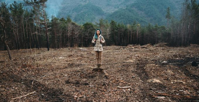 Hiker young woman with backpack standing on wooden stump outdoor