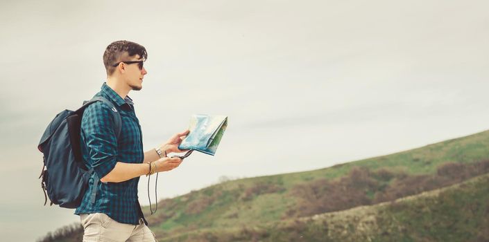 Hiker young man with map and compass searching direction in the mountains in summer outdoor