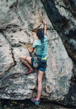 Unrecognizable young woman wearing in safety harness with equipment climbing the rock wall outdoor, rear view