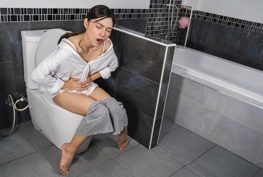 woman sitting on toilet in the bathroom and holding her painful Stomach