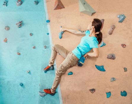 Free climber young woman coating her hand in powder magnesium and climbing artificial boulders indoors