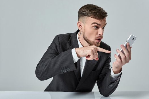 Handsome young man talking on the mobile phone while sitting at his working place in office. Emotions