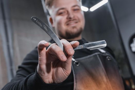 The hand of a barber or professional hairdresser holds a straight tool sharp razor equipment for shaving and beard care, close-up.